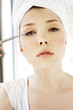 A woman with her hair wrapped up in towel putting on eyeliner.