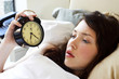 A woman lying on the bed looking at the clock.