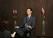 A woman praying in front of a man who is sitting on a shelf meditating.