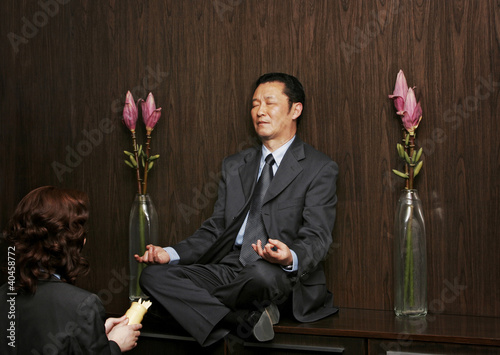 Photo: A woman praying in front of a man who is sitting on a shelf meditating. A woman praying in front of a man who is sitting on a shelf meditating.