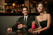 A couple in dinner wear sitting in a bar drinking cocktail.