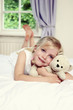 a girl lying forward on the bed with her legs up while hugging her teddy bear.