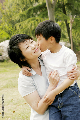 Photo: a boy giving her mother who is holding him in her arms a peck on the cheek. a boy giving her mother who is holding him in her arms a peck on the cheek.
