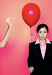 A hand trying to pop a red balloon held by a lady in formal suit.