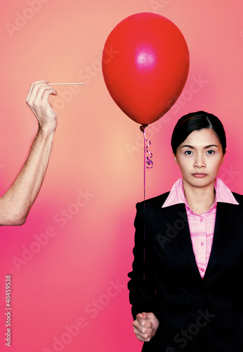 Photo: A hand trying to pop a red balloon held by a lady in formal suit. A hand trying to pop a red balloon held by a lady in formal suit.