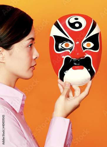 Photo: Side shot of a lady holding a mask facing the camera. Side shot of a lady holding a mask facing the camera.