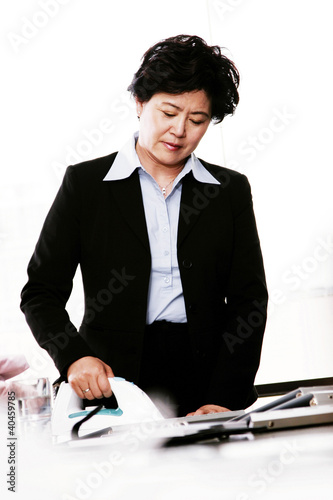 Photo: A woman in office attire ironing clothes. A woman in office attire ironing clothes.