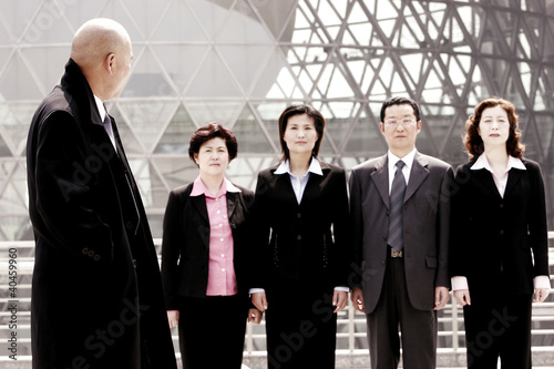 Photo: A bald man watching a group of business people standing in a row. A bald man watching a group of business people standing in a row.