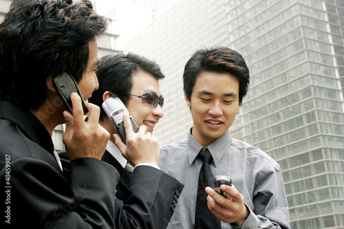 Photo: Three men in office attires using handphones. Three men in office attires using handphones.