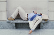 Man sleeping on the bench with newspaper covering his face.