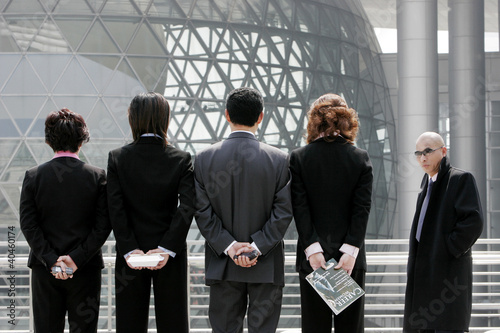 Photo: Back shot of business man and women standing in a row hiding their stuff. Back shot of business man and women standing in a row hiding their stuff.