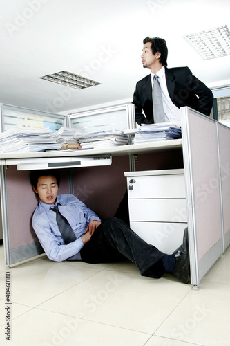 Photo: Man trying to find his worker who is sleeping under the desk. Man trying to find his worker who is sleeping under the desk.