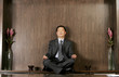 Man in business suit sitting on the shelf meditating. 