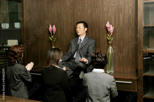 Photo: Women worshipping a businessman who is sitting on the shelf meditating. Women worshipping a businessman who is sitting on the shelf meditating.