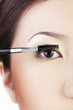 Woman applying mascara on her lashes.