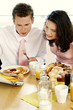 Couple reading newspaper while having breakfast together.