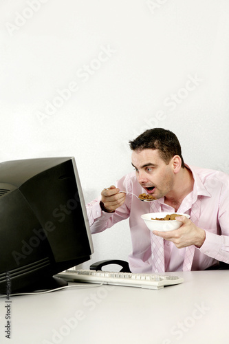 Photo: Businessman checking his work while eating breakfast cereal. Businessman checking his work while eating breakfast cereal.