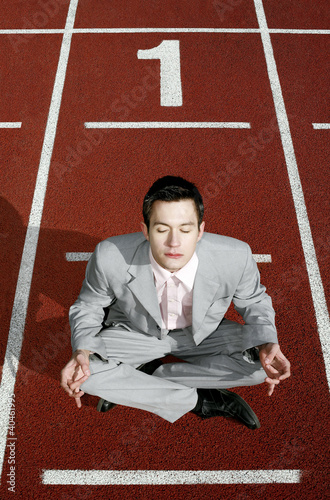 Photo: Businessman meditating on a running track. Businessman meditating on a running track.