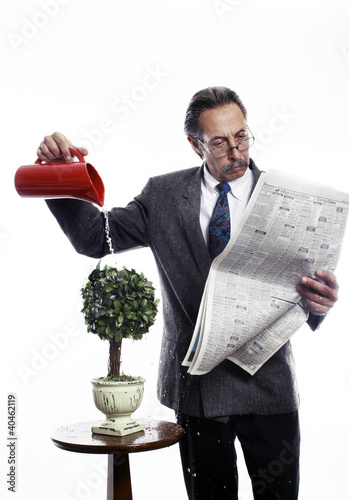 Photo: Businessman reading newspaper while watering the plants. Businessman reading newspaper while watering the plants.