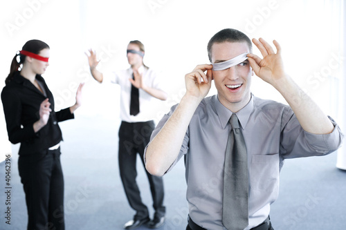 Photo: Businessman cheating during a blindfolding game. Businessman cheating during a blindfolding game.