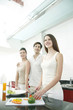 Woman cutting vegetables in the kitchen with her friends beside her