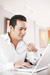 Man holding his glasses while using laptop