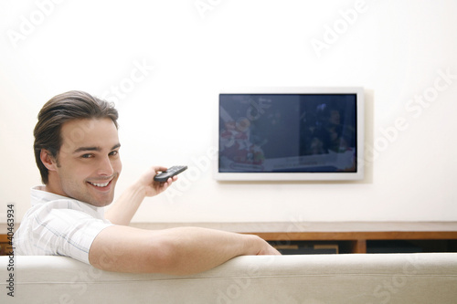 Foto: Man sitting on the couch holding a television remote control Man sitting on the couch holding a television remote control