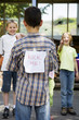 Children laughing at boy with a kick me sign on his back