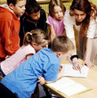 Female teacher pointing at a book with students surrounding her