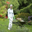 Senior woman pushing a wheelbarrow of plants in the garden
