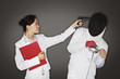 Businesswoman pointing a gun at man in fencing suit and mask