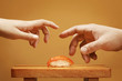Two hands trying to take a sushi