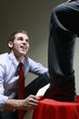 Businessman polishing another businessman's shoe