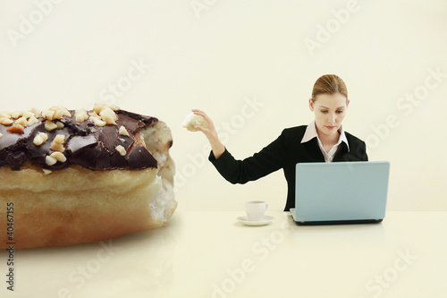 Foto: Businesswoman pulling out a chunk of doughnut while using laptop Businesswoman pulling out a chunk of doughnut while using laptop