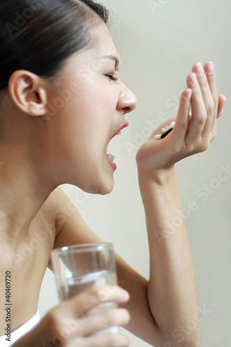 Photo: Woman eating pills while holding a glass of water Woman eating pills while holding a glass of water