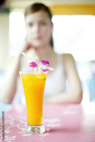 Foto: Focus on a glass of fruit juice with woman sitting in the background Focus on a glass of fruit juice with woman sitting in the background