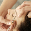 Hand tweezing woman's eyebrow