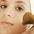 Hand applying powder foundation on woman's cheek