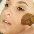 Hand applying powder foundation on woman's cheek