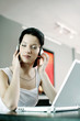 Woman listening to music on the headphones while using laptop
