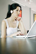 Photo: Woman listening to music on the headphones while using laptop Woman listening to music on the headphones while using laptop