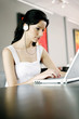 Photo: Woman listening to music on the headphones while using laptop Woman listening to music on the headphones while using laptop