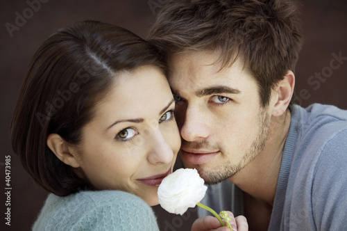 Photo: Couple smiling at the camera while holding a white rose Couple smiling at the camera while holding a white rose