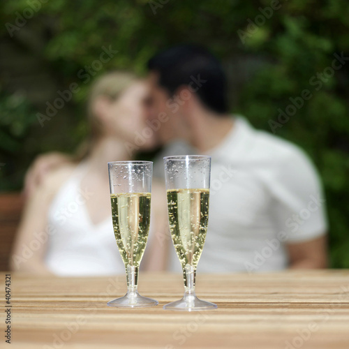 Photo: Two glasses of champagne with couple kissing in the background Two glasses of champagne with couple kissing in the background