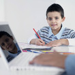 Boy doing homework while his father using laptop
