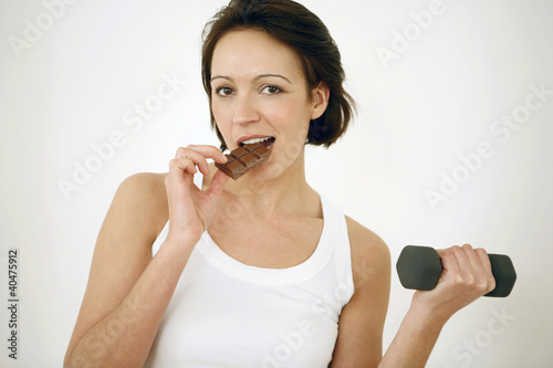 Photo: Woman eating chocolate bar while lifting dumbbell Woman eating chocolate bar while lifting dumbbell