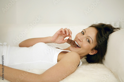 Photo: Woman lying on the couch eating chocolate bar Woman lying on the couch eating chocolate bar
