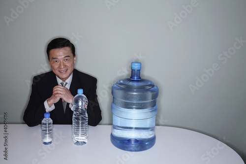 Photo: Businessman smiling at the camera with three water bottles on the table Businessman smiling at the camera with three water bottles on the table