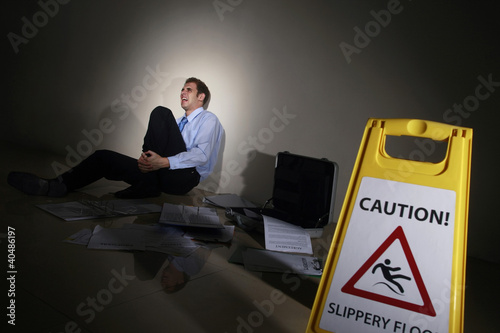 Photo: Businessman slipped beside Caution sign, holding onto his leg Businessman slipped beside Caution sign, holding onto his leg