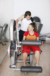 Woman exercising on gym equipment, personal trainer assisting her